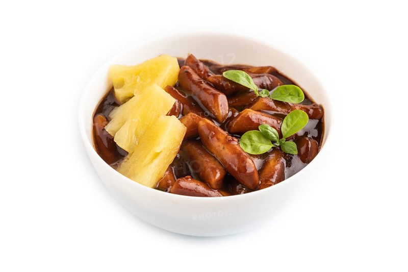 Tteokbokki or Topokki, fried rice cake stick, popular Korean street food with spicy jjajang sauce and pineapple isolated on white background. Side view