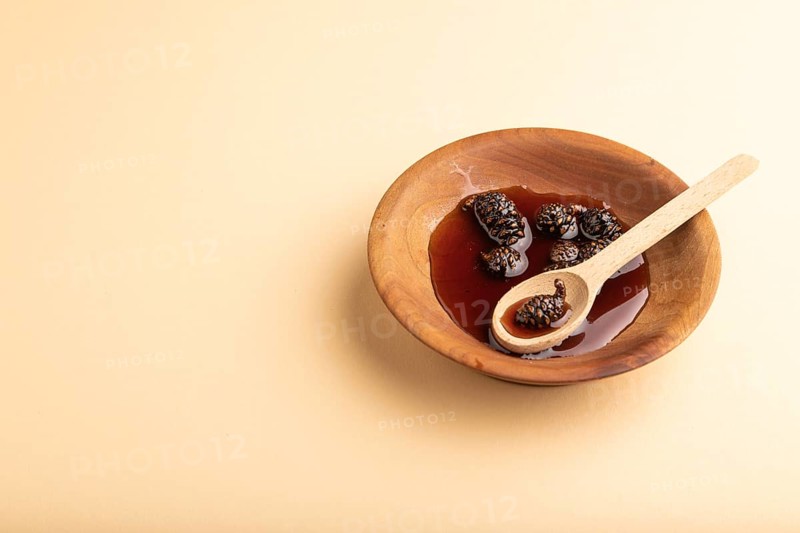 Pine cone jam in wooden bowl on orange pastel background. Side view, copy space