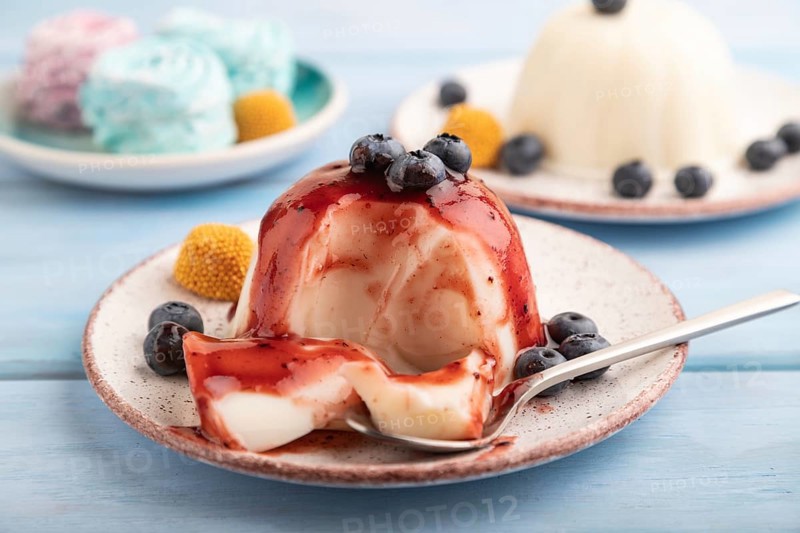 White milk jelly with blueberry jam on blue wooden background and blue linen textile. side view, close up, selective focus