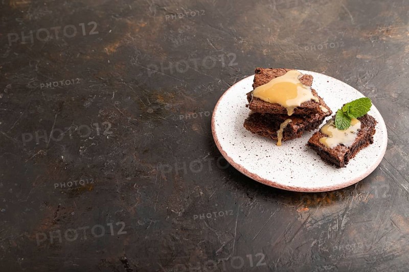 Chocolate brownie with caramel sauce with a cup of coffee on black concrete background. side view, copy space