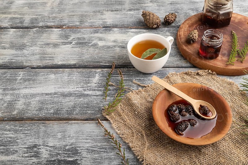 Pine cone jam with herbal tea on gray wooden background and linen textile. Side view, copy space