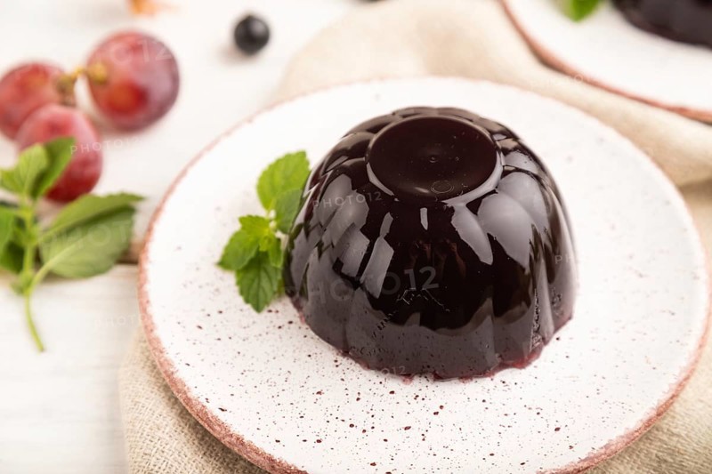 Black currant and grapes jelly on white wooden background and linen textile. side view, close up, selective focus