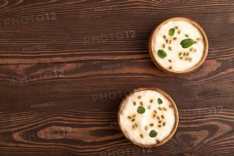Yoghurt with granadilla and mint in wooden bowl on brown wooden background. top view, flat lay, copy space
