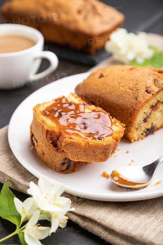 Homemade cake with raisins, almonds, soft caramel and a cup of coffee on a black concrete background and linen textile. Side view, close up, selective focus