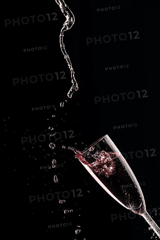 Drops and splashes fly from a champagne glass with rose sparkling wine on a black background