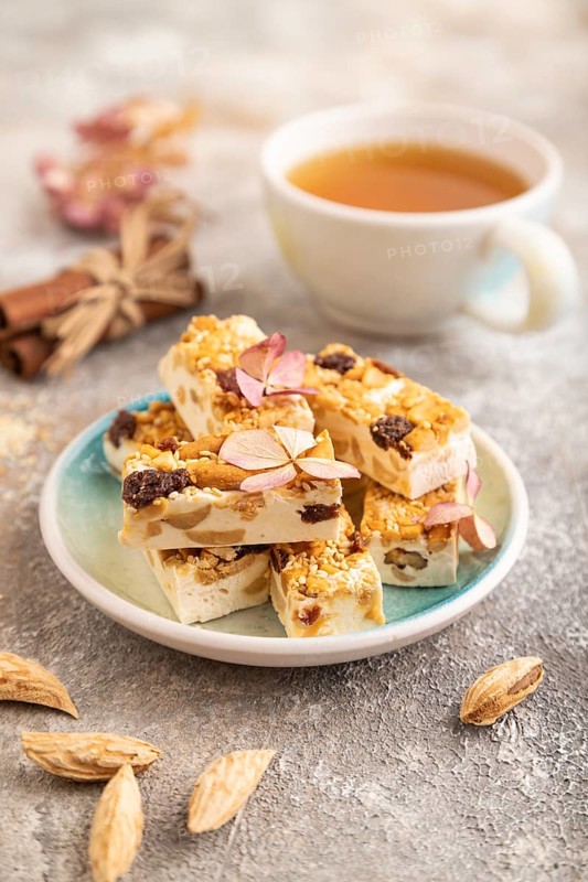 Traditional candy nougat with nuts and sesame with cup of green tea on brown concrete background. side view, close up, selective focus