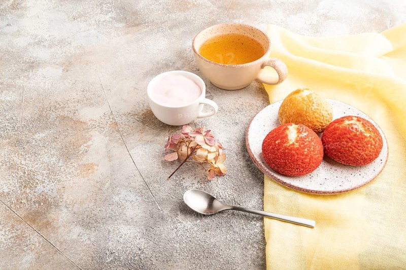 Traditional french custard dessert shu cake and cup of green tea on brown concrete background and yellow linen textile. side view, copy space. Breakfast, morning, concept
