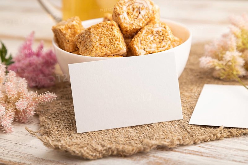 White business card with traditional turkish delight (rahat lokum) in white ceramic bowl on a white wooden background. side view, close up