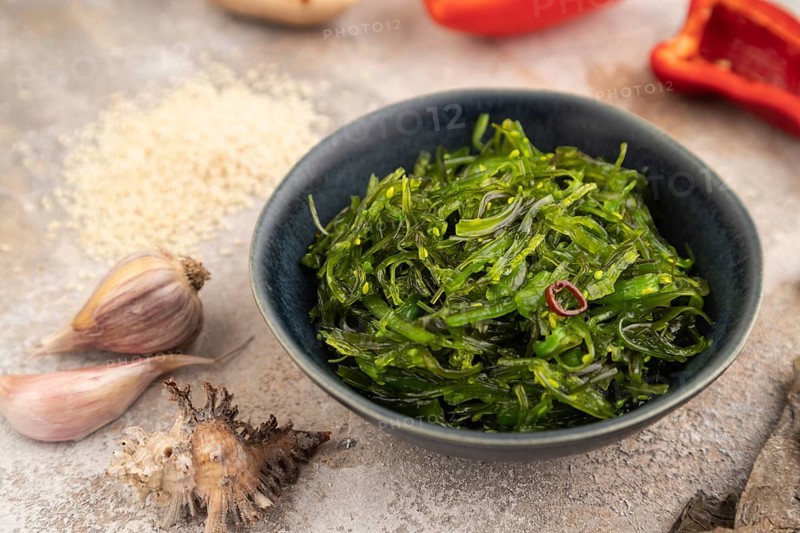 Chuka seaweed salad in blue ceramic bowl on brown concrete background. Side view, close up, selective focus