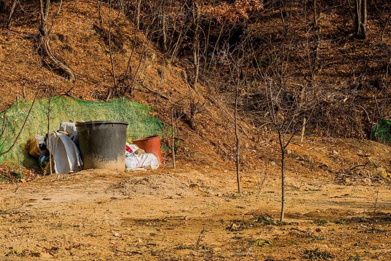 Daejeon, South Korea, January 24, 2020: Two large brown plastic tubs next to bags of fertilizer in field of young trees in wilderness. For editorial use only, Asia