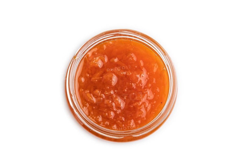 Carrot jam with cinnamon in glass jar isolated on white background. Top view, flat lay, close up