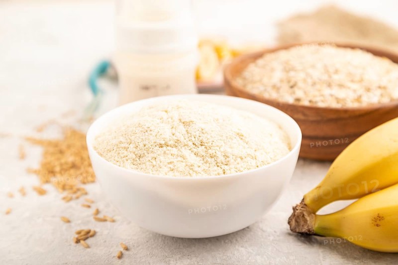 Powdered milk and oatmeal, banana baby food mix, infant formula, pacifier, bottle, spoon on gray concrete background. Side view, close up, selective focus, artificial feeding concept