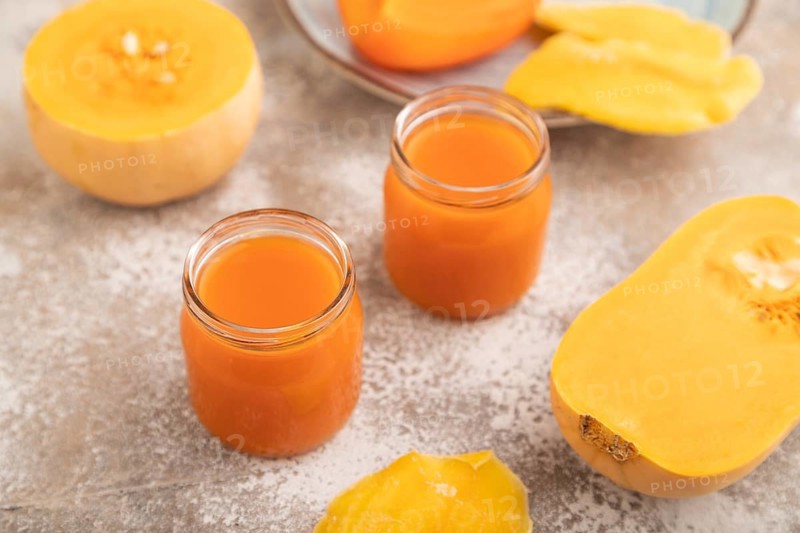 Baby puree with fruits mix, pumpkin, persimmon, mango infant formula in glass jar on brown concrete background. Side view, close up, selective focus, artificial feeding concept