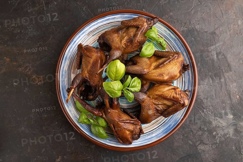 Smoked quails with herbs and spices on a ceramic plate on a black concrete background. Top view, flat lay, close up