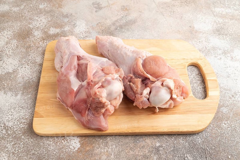 Raw turkey wing with herbs and spices on a wooden cutting board on a brown concrete background. Side view, close up