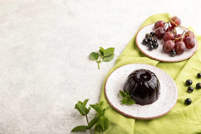 Black currant and grapes jelly on gray concrete background and green linen textile. side view, copy space