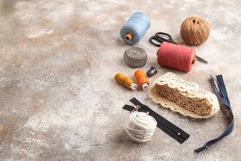Sewing accessories: scissors, thread, thimbles, braid on brown concrete background. Side view, copy space