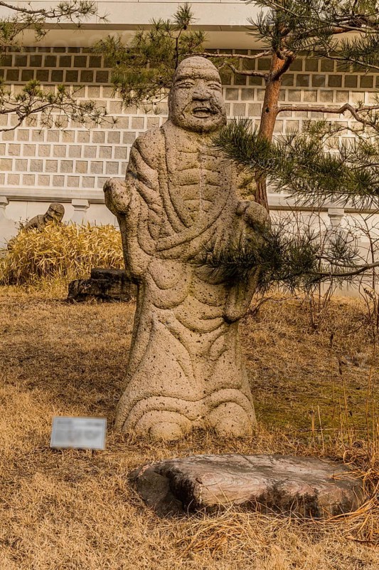 Stone carved statue of Buddhist deity kanakavatsa in front of white wall in garden in South Korea