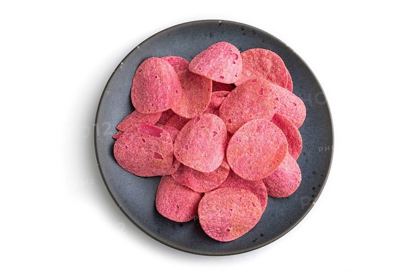 Red potato chips with herbs and tomatoes on blue cearmic plate isolated on white background. Top view, flat lay, close up