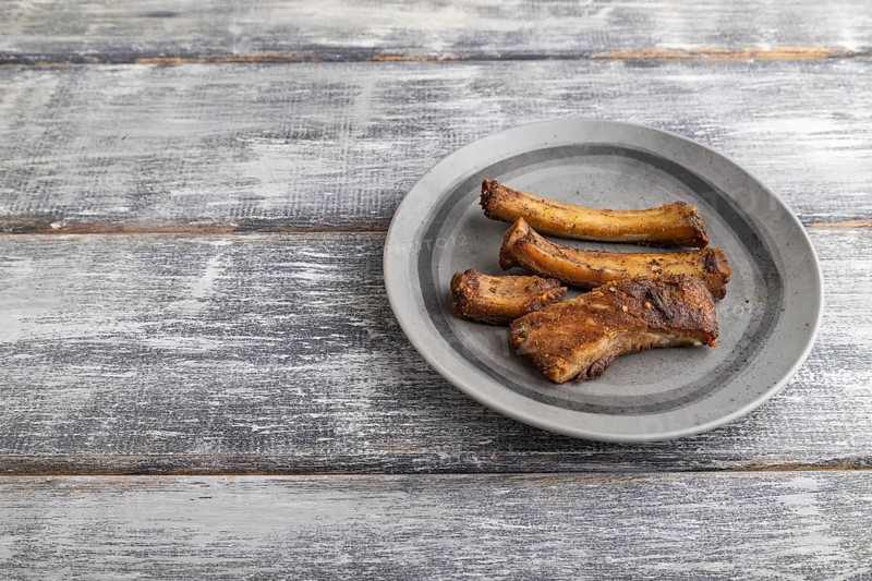 Pork ribs on a wooden plate on a gray wooden background. Side view, close up, copy space