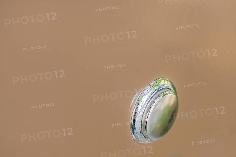 Closeup of silver metallic push button switch used to turn on power to machine on soft brown background