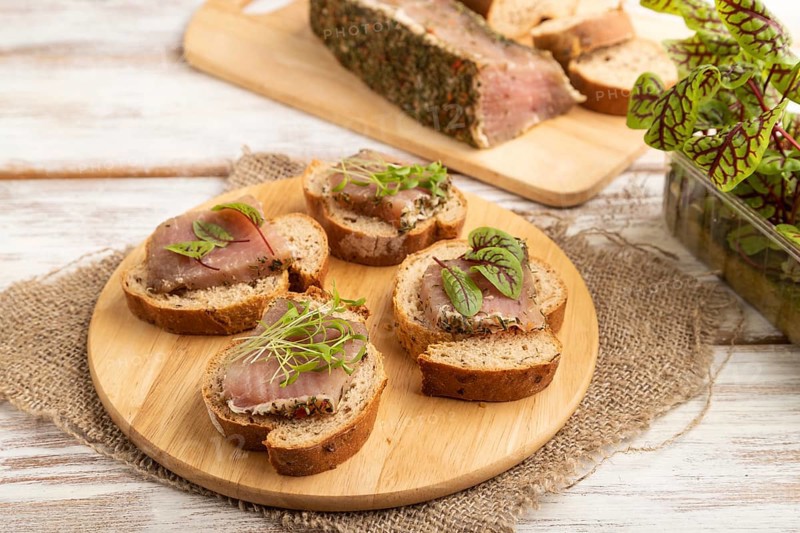Bread sandwiches with jerky salted meat, sorrel and cilantro microgreen on white wooden background and linen textile. side view, close up