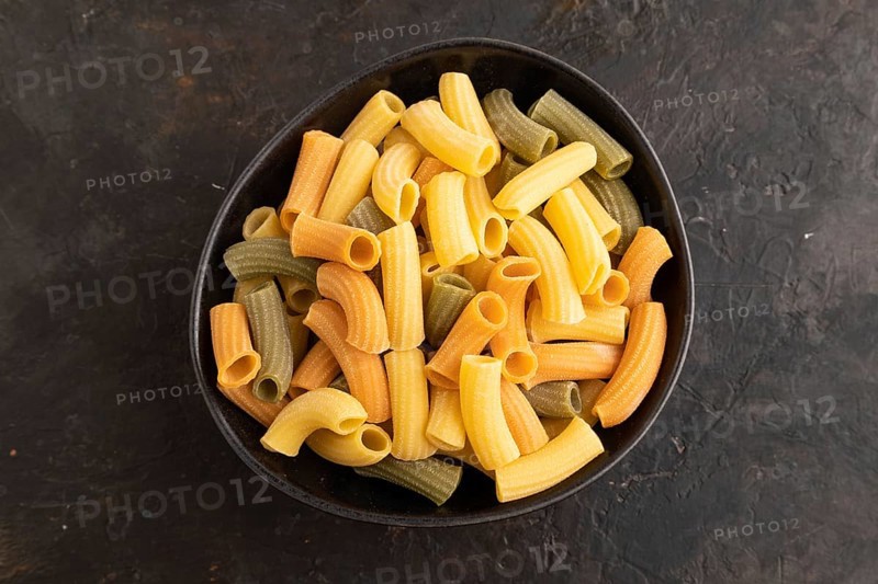 Rigatoni colored raw pasta with tomato, eggs, spices, herbs on black concrete background. Top view, flat lay