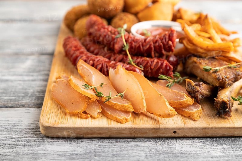 Set of snacks: sausages, fried potatoes, meat balls, dumplings, basturma on a cutting board on a gray wooden background. Side view, close up, selective focus