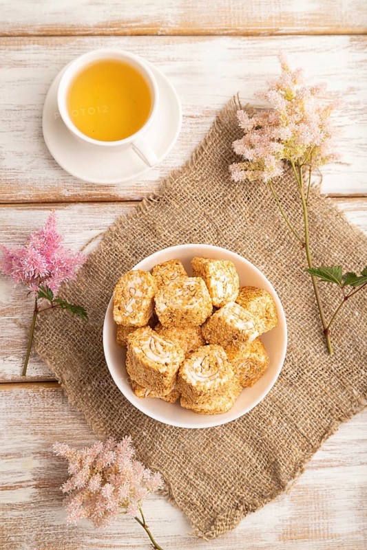 Traditional turkish delight (rahat lokum) in white ceramic plate with cup of green tea on a white wooden background. top view, flat lay, close up
