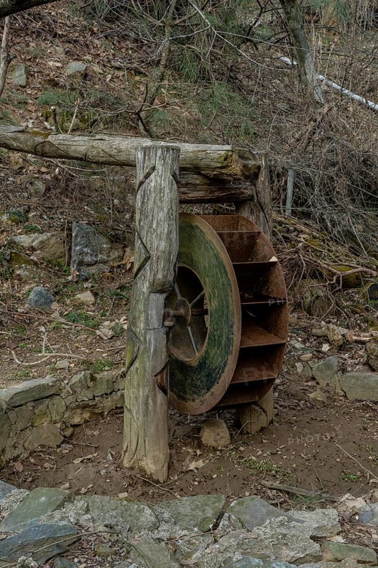 Old, rusted, metal waterwheel in mountainside public park