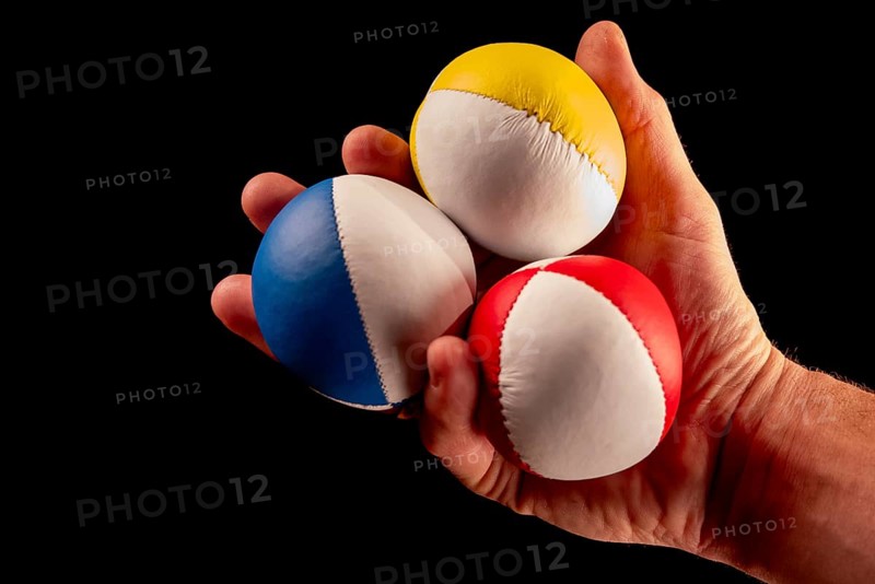 Male hand holding 3 colourful juggling balls, black background, studio shot, Germany, Europe