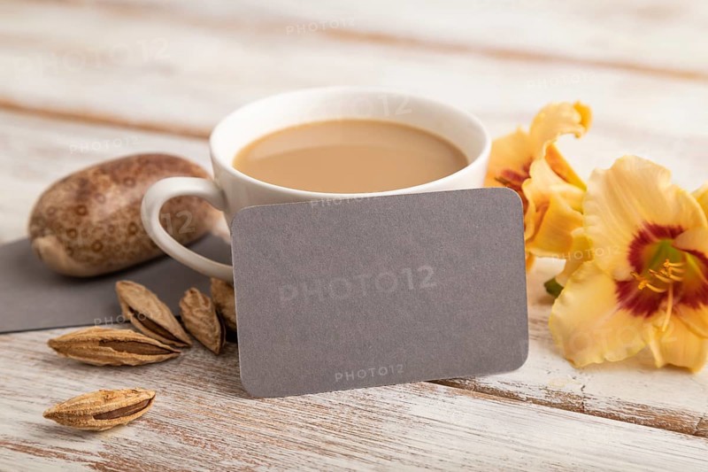 Gray paper business card mockup with orange day-lily flower and cup of coffee on white wooden background. Blank, side view, copy space, still life. spring concept