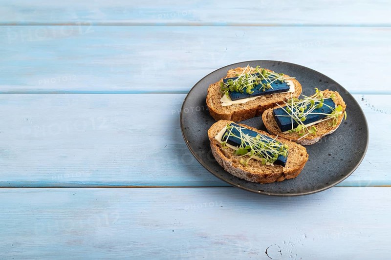 Bread sandwiches with blue lavender cheese and mustard microgreen on blue wooden background. side view, copy space