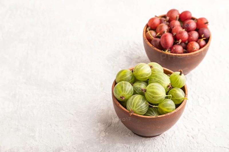 Fresh red and green gooseberry in clay bowl on gray concrete background. side view, copy space