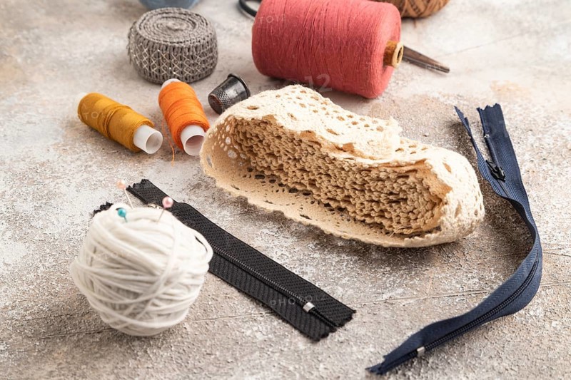 Sewing accessories: scissors, thread, thimbles, braid on brown concrete background. Side view, close up