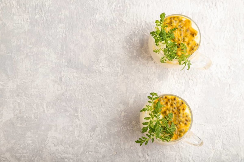 Yogurt with passionfruit and marigold microgreen in glass on gray concrete background. Top view, flat lay, copy space