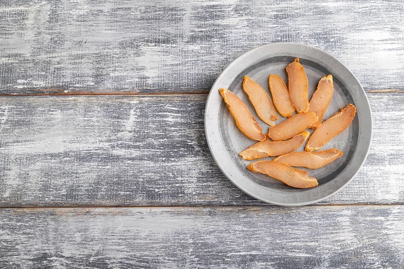 Salted meat on a wooden plate on a gray wooden background. Top view, flat lay, close up, copy space