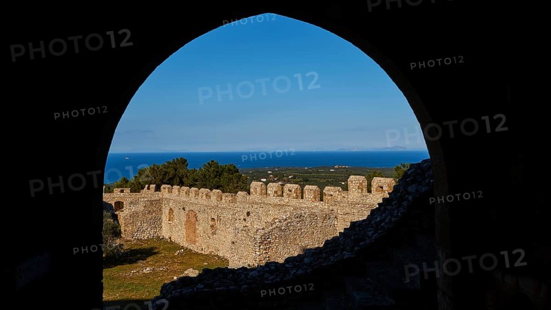 View through a stone arch onto historic fortress walls with blue sky and sea in the background, Chlemoutsi, High Medieval Crusader Castle, Kyllini Peninsula, Peloponnese, Greece, Europe