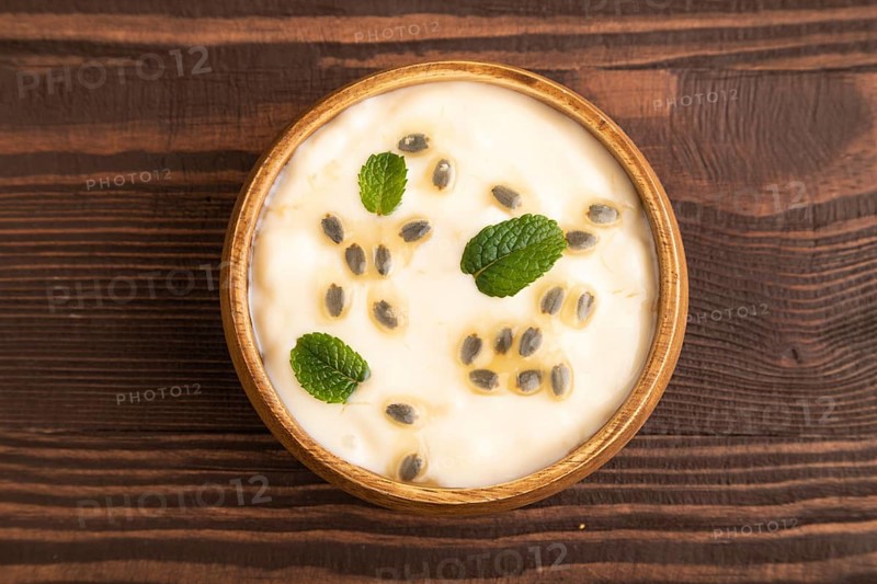 Yoghurt with granadilla and mint in wooden bowl on brown wooden background. top view, flat lay, close up