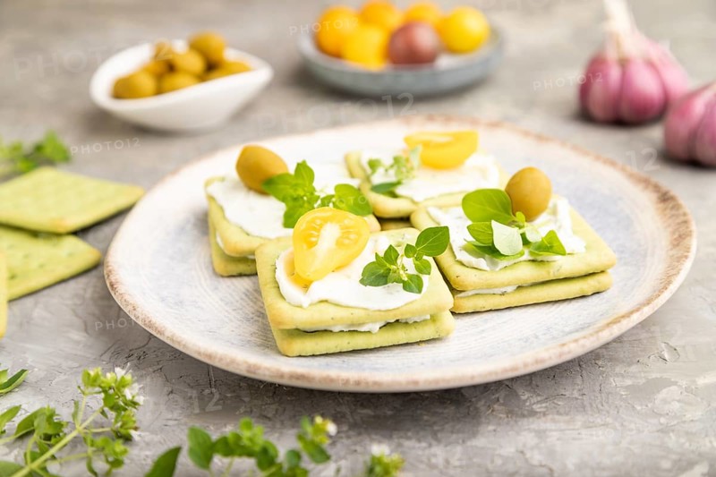 Green cracker sandwiches with cream cheese and cherry tomatoes on gray concrete background. side view, close up, selective focus