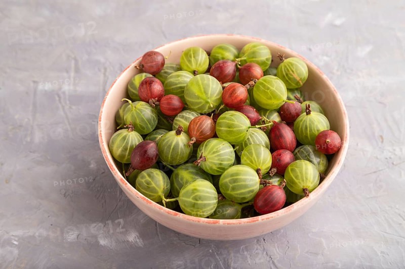 Fresh red and green gooseberry in ceramic bowl on gray concrete background. side view, close up