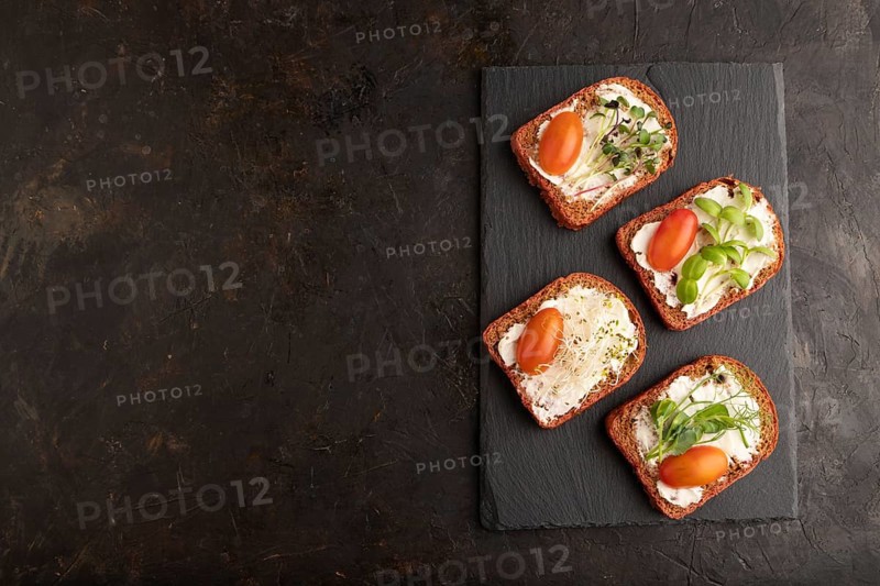 Red beet bread sandwiches with cream cheese, tomatoes and microgreen on black concrete background. top view, flat lay, copy space