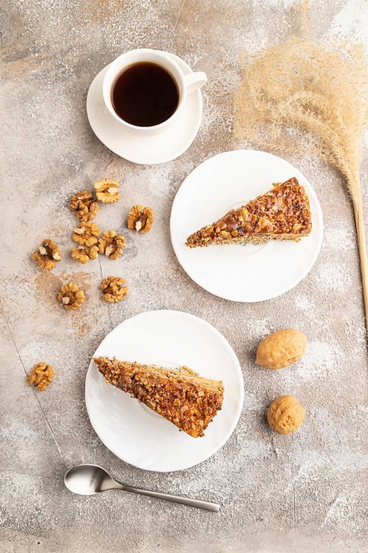 Walnut and hazelnut cake with caramel cream, cup of coffee on brown concrete background. top view, flat lay