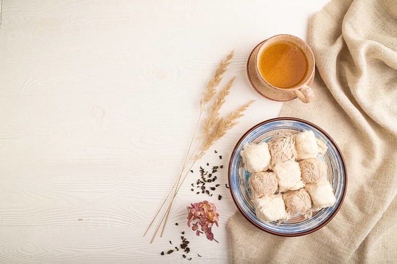Traditional arabic sweets pishmanie and a cup of green tea on white wooden background and linen textile. top view, flat lay, copy space