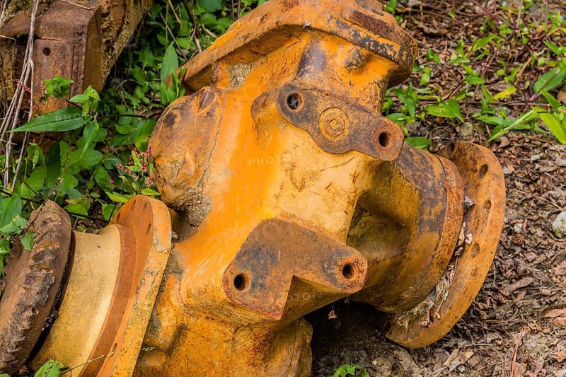 Closeup of broken down bulldozer trans-axle laying in weeds on ground