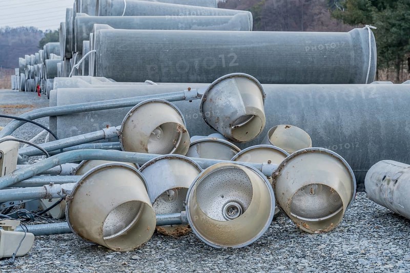 Old dirty street light fixtures laying on gravel in front of culverts at construction site