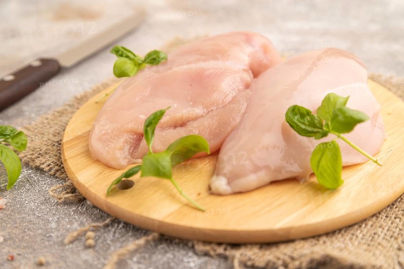 Raw chicken breast with herbs and spices on a wooden cutting board on a brown concrete background. Side view, close up, selective focus