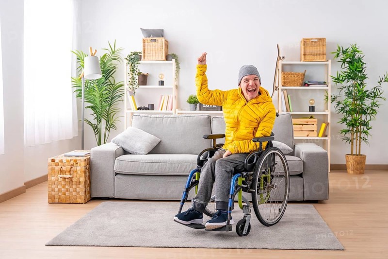 Portrait with copy space of a disabled man in wheelchair celebrating raising fist at home
