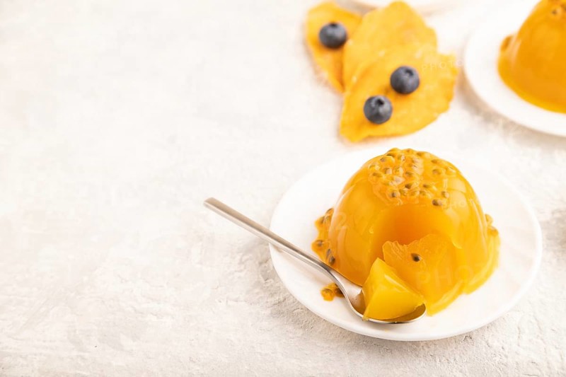 Mango and passion fruit jelly with blueberry on gray concrete background and linen textile. side view, copy space