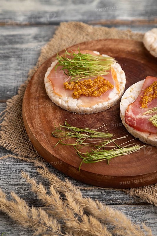 Puffed rice cake sandwiches with jerky salted meat, carrot microgreen on gray wooden background and linen textile. side view, close up, selective focus